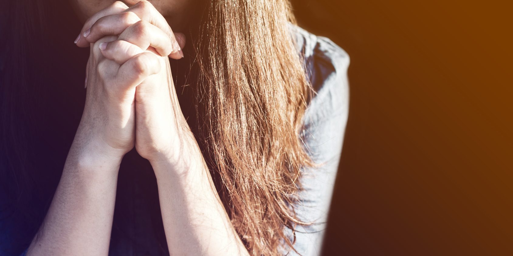 Woman praying in meadow at sunset