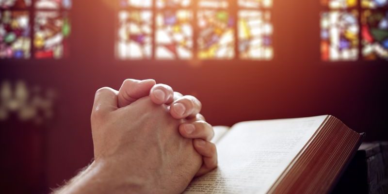 Hands folded in prayer on a Holy Bible in church concept for fai