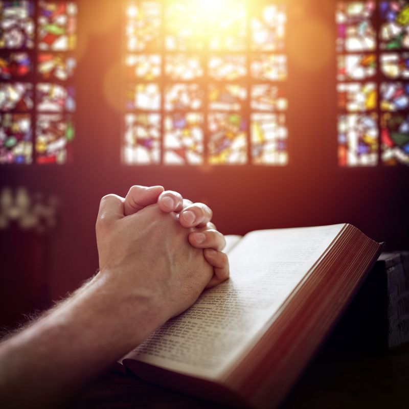 Hands folded in prayer on a Holy Bible in church concept for fai