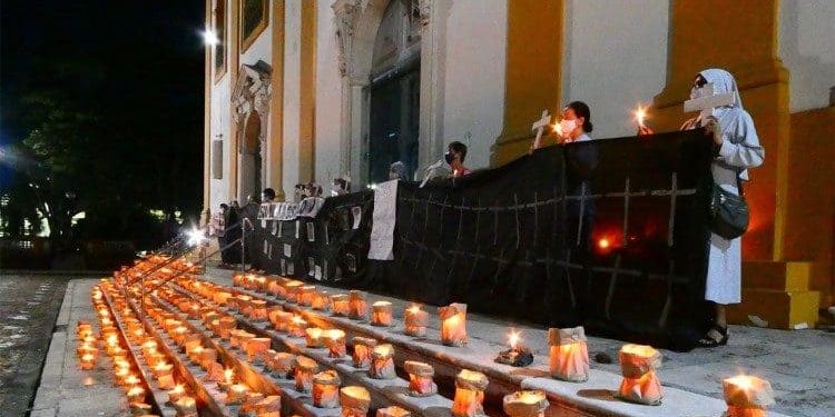 manaus-500-mil-mortos Velas acesas nos degraus da Arquidiocese de Manaus; religiosas católicas estão no primeiro degrau, usando máscaras e segurando cruzes de madeira.