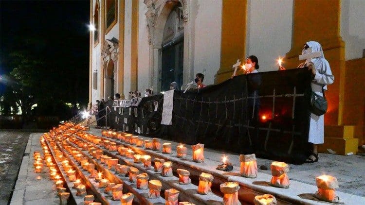 manaus-500-mil-mortos Velas acesas nos degraus da Arquidiocese de Manaus; religiosas católicas estão no primeiro degrau, usando máscaras e segurando cruzes de madeira.