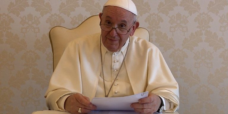 papa-gratidao-trabalho-solidario-de-mar-del-plata Papa Francisco segura papel sobre mesa de madeira enquanto olha para a câmera.