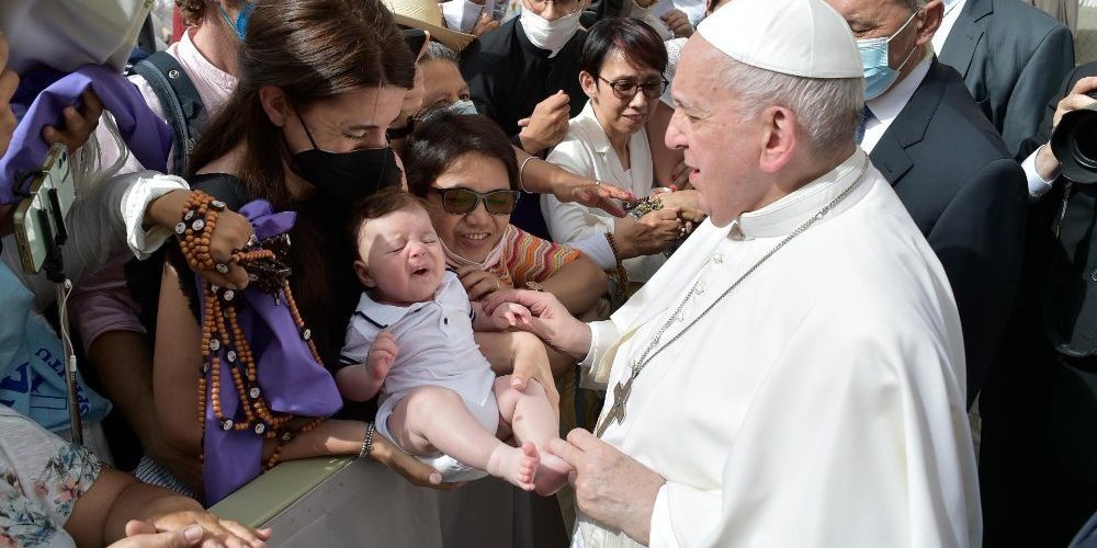 papa-jesus-verdade Papa cumprimentando um grupo de pessoas enquanto segura a perna de um bebê que está no colo de uma mulher usando máscara preta.