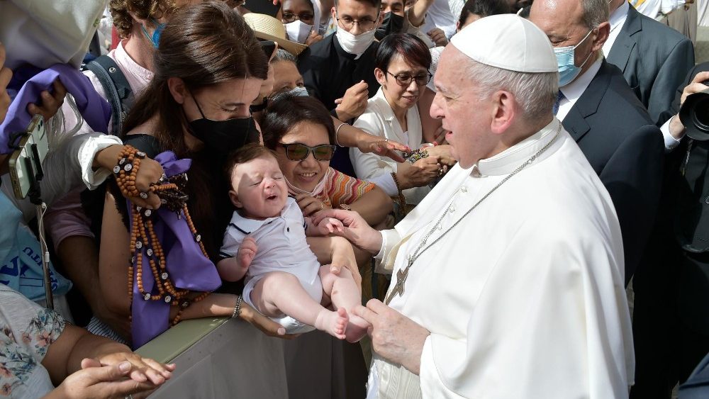 papa-jesus-verdade Papa cumprimentando um grupo de pessoas enquanto segura a perna de um bebê que está no colo de uma mulher usando máscara preta.