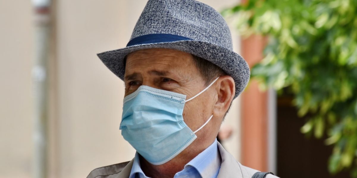 Homem idoso usando máscara e chapéu.