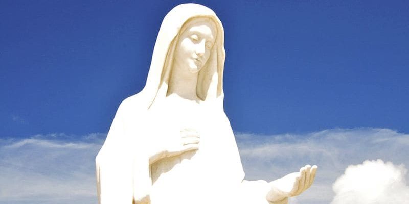 Estátua da Virgem Maria em Medjugorje na frente de um céu azul com nuvens brancas
