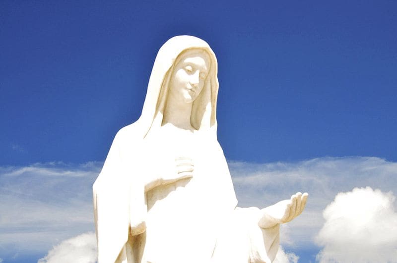 Estátua da Virgem Maria em Medjugorje na frente de um céu azul com nuvens brancas
