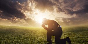 240_F_51694403_N4567tOF7psOJlaUZsaxRiHZmVL7hdcu Homem ajoelhado diante céu com nuvens e feixe de luz do sol