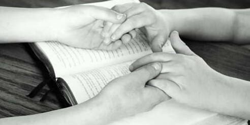 casal-orando Duas pessoas de mãos dadas em cima de uma Bíblia
