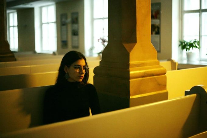 consagracao-eucaristia Mulher de preto sentada em banco de igreja.