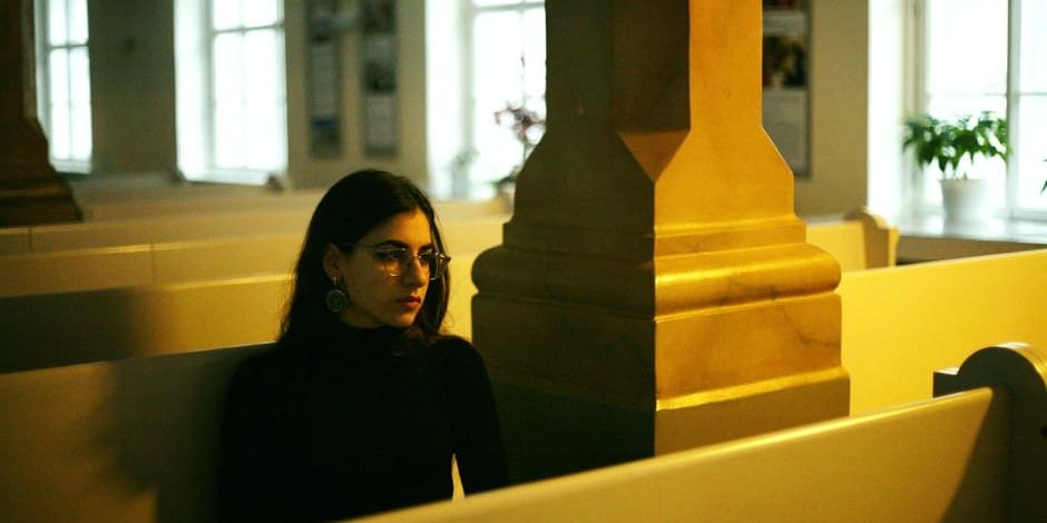 consagracao-eucaristia Mulher de preto sentada em banco de igreja.