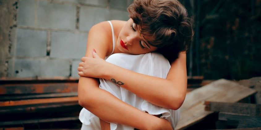 Mulher de aparência abatida com a cabeça apoiada nos joelhos.