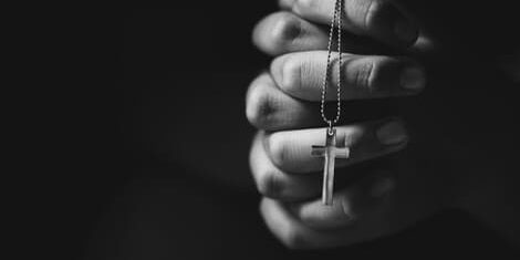 oracao-terco Mãos em posição de oração segurando um terço; imagem em preto e branco