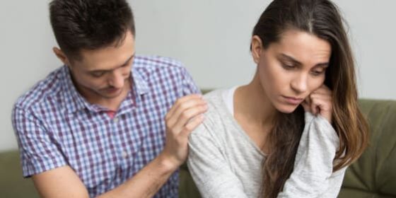 Homem segurando nos ombros de mulher enquanto ela está de cabeça baixa e levemente inclinada para o lado oposto