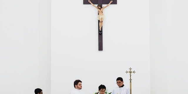 pexels-marcelo-chagas-1782330 (1) Sacerdote usando microfone na frente de uma parede branca com a imagem de Jesus crucificado