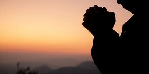 Silhueta de menina rezando na frente de um pôr do sol