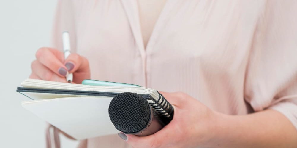 Mulher escrevendo em bloco de notas e segurando microfone