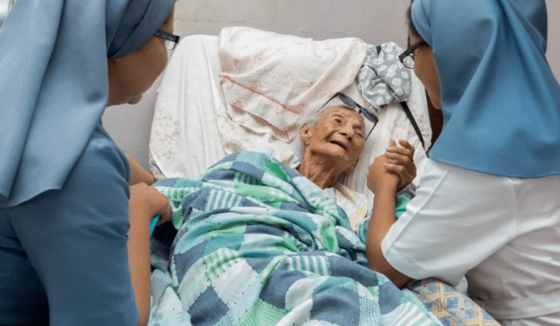 Duas irmãs religiosas amparando idosa em cama de hospital